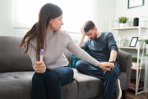 Casal com semblante triste e mulher segurando teste de gravidez