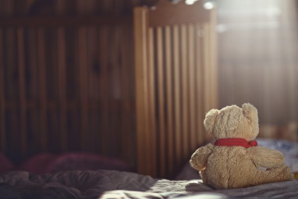 Ursinho de pelúcia em cima de cama em quarto vazio e escuro