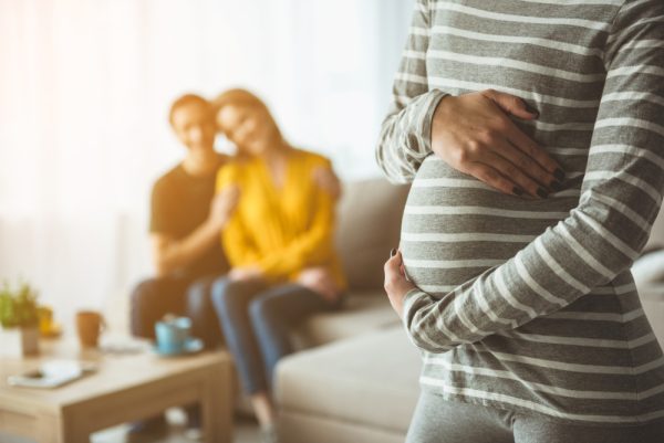 Casal sentado em sofá e olhando para mulher grávida