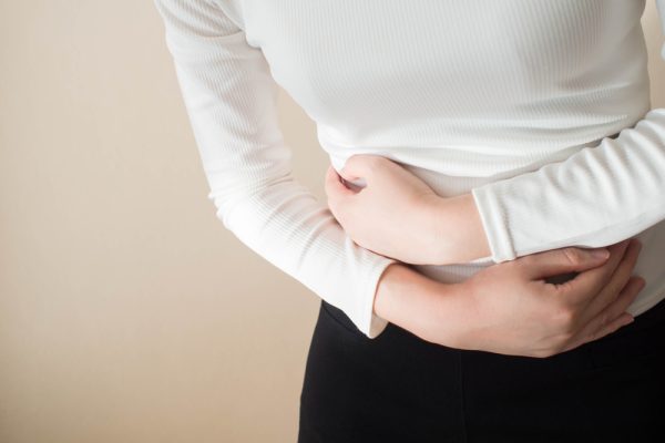 Abdômen de uma mulher que veste uma camisa branca com uma dor evidente na região do abdômen.