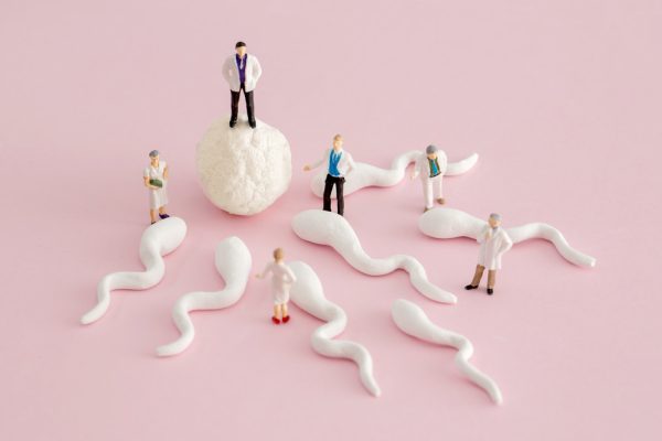 Ilustração de espermatozoides indo em direção a um óvulo. No meio, há algumas miniaturas de médicos.