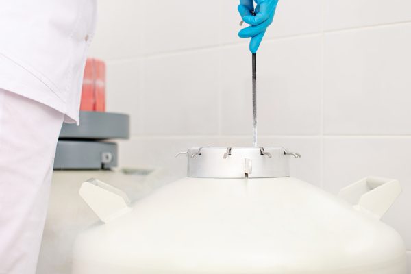 Médico com luva inserindo um frasco em um tanque de nitrogênio.