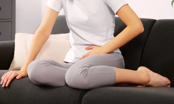 Mulher sentada em sofá com dor causada pela doença inflamatória pélvica