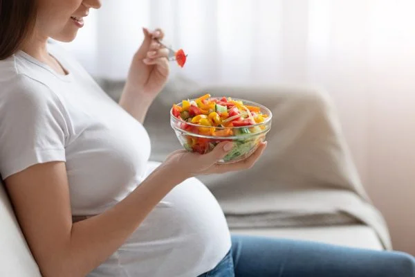 Mulher grávida comendo verduras em um pote de vidro.