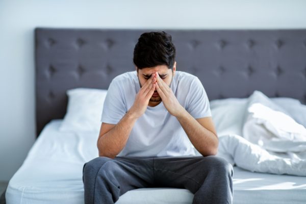 Homem sentado na beira da cama preocupadp.