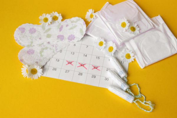 Absorventes e tampões menstruais no calendário do período menstrual com camomilas em fundo amarelo.