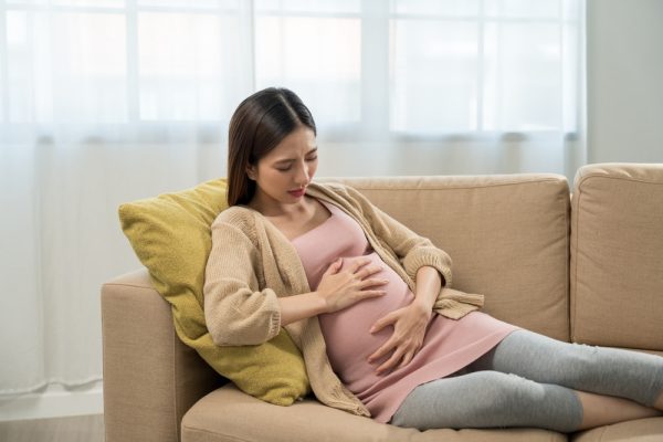 Mulher grávida preocupada, deitada em sofá.