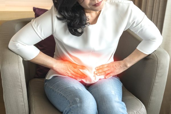 Mulher sentada em poltrona com as mãos na barriga, sentindo dores.