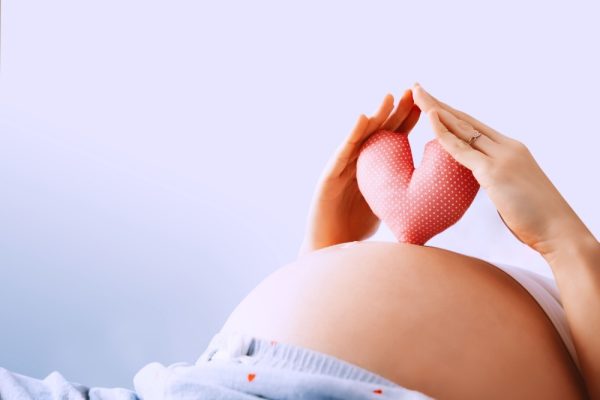 Mulher grávida segurando protótipo de coração em cima da barriga