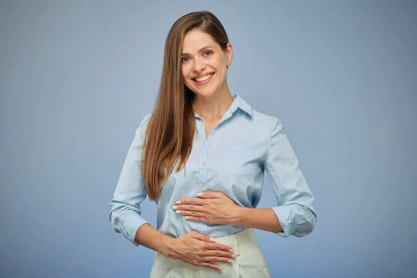 Mulher sorrindo com a mão na barriga ilustrando sintomas após transferência de embriões.