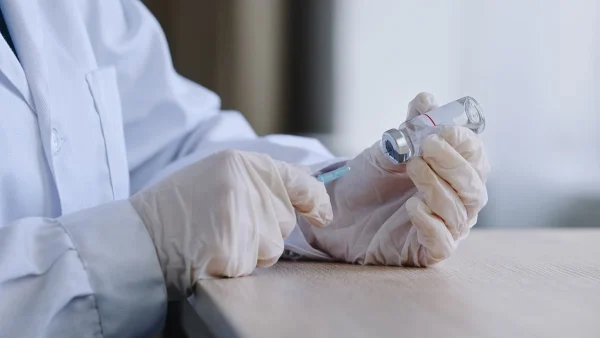Médico retirando medicamento de frasco com seringa representando uso de medicamentos para estímulo ovariano.