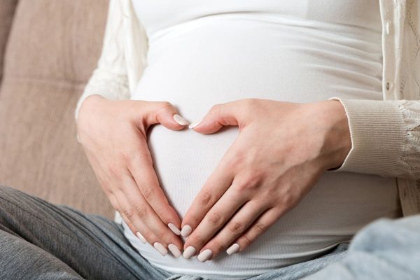 Mulher grávida fazendo coração com as mãos sobre a barriga representando gravidez após miomectomia.