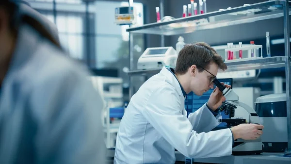 Médico analisando material no microscópio ilustrando estudo no protocolo MAGENTA.