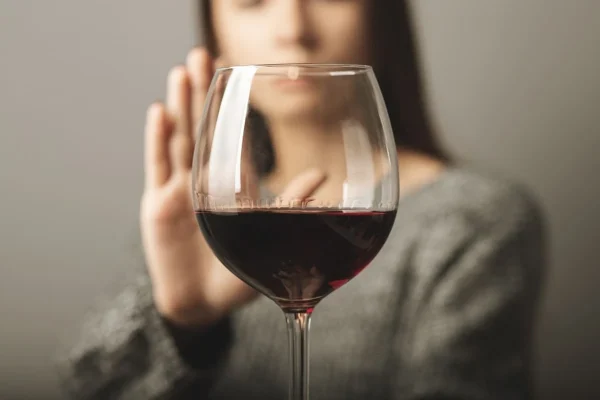 Mulher fazendo gesto de recusa ao lado de taça de vinho representando a relação entre álcool e a FIV.