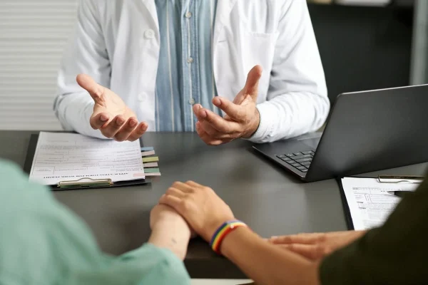 Duas mulheres de mãos dadas em consulta com médico representando FIV para casal homoafetivo.