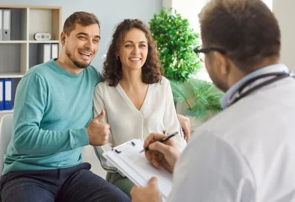 Casal sorridente em consulta com médico representando tratamentos para engravidar.